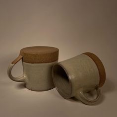 two coffee mugs sitting next to each other on a white surface with brown handles