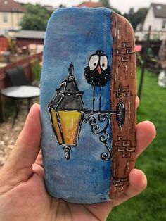 a hand holding up a painted rock with a bird on it and a street light