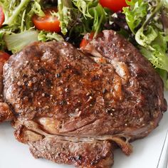 a piece of steak next to a salad on a white plate