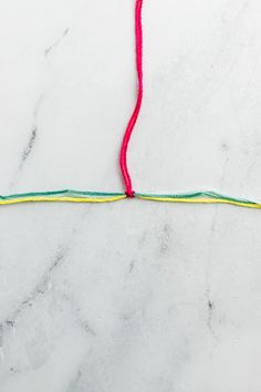 a piece of string that is on top of a marble surface with red and green thread