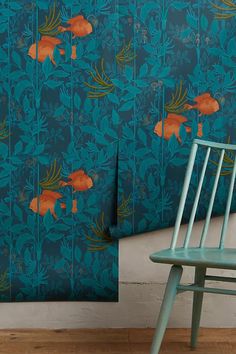 a chair sitting in front of a blue wall with orange fish and plants on it