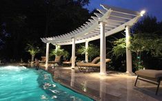 an outdoor swimming pool at night with lounge chairs and pergolated canopy over it