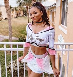 a woman in a cheerleader outfit standing on a porch next to a fence and palm trees