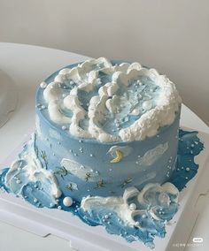 a blue cake with white frosting and clouds on top is sitting on a table