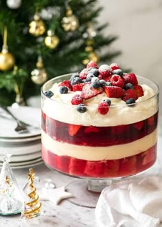 a red, white and blue trifle in a glass dish next to a christmas tree