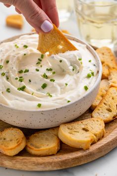 a person dipping a tortilla chip into a bowl of white dip surrounded by crackers