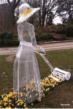 a woman in a white dress and hat with a lawn mower next to flowers