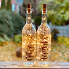 two wine bottles with lights in them sitting on a table