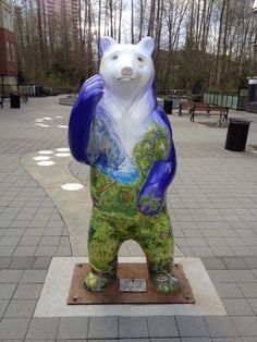 a statue of a bear is on display in a public area with trees and buildings behind it