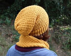 a woman wearing a yellow knitted hat and scarf on top of her head with trees in the background