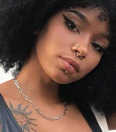 a close up of a person with an afro and piercing on her nose, wearing a black tank top