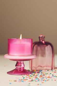 a pink candle sitting on top of a cake plate next to a glass container filled with sprinkles