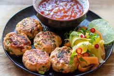 a black plate topped with meatballs and vegetables next to a bowl of dipping sauce