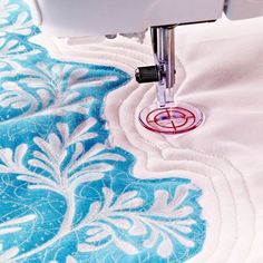 the sewing machine is working on the blue and white fabric with floral designs in it