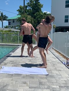 two men in swim trunks are standing on a towel by the pool while another man is holding his arm around him