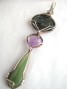 three stone pendants are sitting on a white tablecloth, one is green and the other is purple