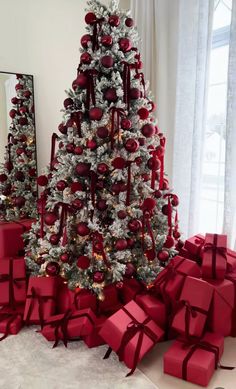 a christmas tree with red and silver presents under it next to a mirror in a room