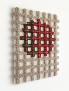 a piece of art made out of wool with red and black squares on the wall