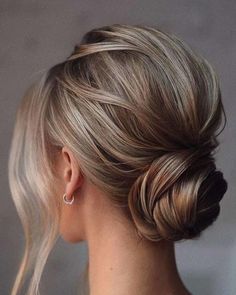 a woman with blonde hair styled into a low bun, wearing a white shirt and earrings