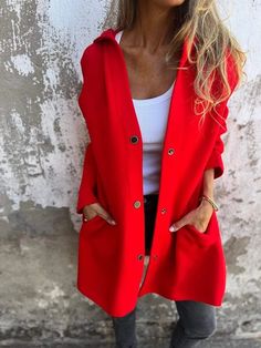 a woman standing against a wall wearing a red coat