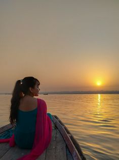 a woman sitting on the end of a boat looking out at the water as the sun sets