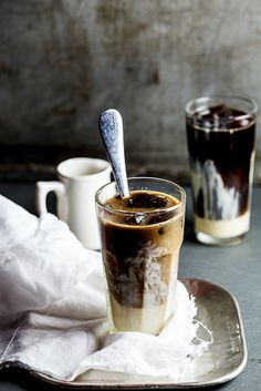 two glasses filled with liquid sitting on top of a plate next to cups and spoons