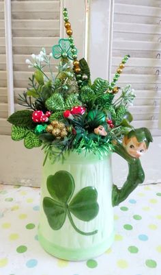 a green vase filled with lots of flowers and greenery on top of a table