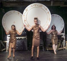 three women in gold dresses holding large plates