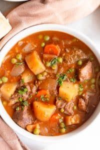 a white bowl filled with stew next to two slices of bread on top of a table