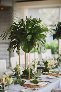 the table is set with place settings and greenery in gold vases, along with plates and napkins