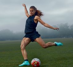 a woman kicking a soccer ball on top of a field