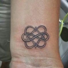 a small tattoo on the wrist with an intertwined knot in the middle and two hearts at the center