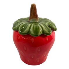 a ceramic red pepper with green leaves on it's top, sitting in front of a white background