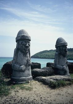 two stone statues sitting next to each other near the ocean