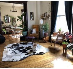 a living room filled with lots of furniture and plants on top of a hard wood floor