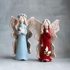 two ceramic angel figurines sitting next to each other on a white surface with grey background