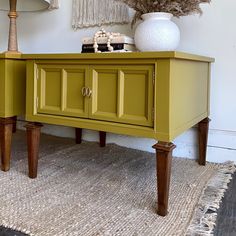 a yellow cabinet sitting on top of a rug next to a white vase and lamp