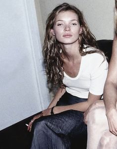 two women sitting next to each other on a couch in front of a white wall