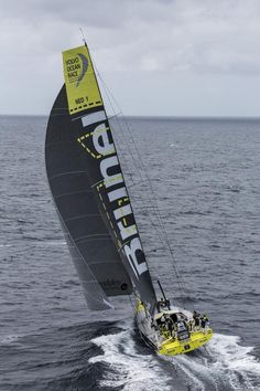 a yellow and black sail boat in the ocean with people on it's side