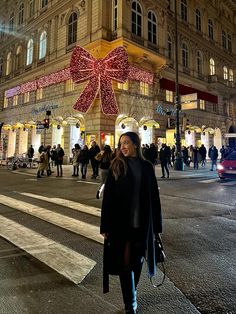 a woman walking down the street in front of a large building with lights on it