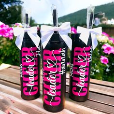 three black and pink wine bottles with white bows on them sitting on a wooden table