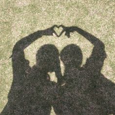 two people making a heart shape with their hands on the grass in front of them