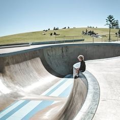 a skateboarder is sitting on the edge of a half pipe at a skate park