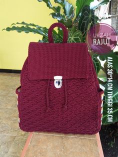 a red crocheted backpack sitting on top of a wooden table next to a potted plant