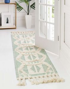 a white door with a green rug on the floor and a potted plant next to it