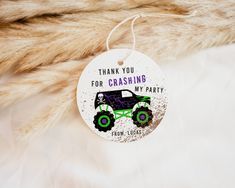 a white ornament with a green monster truck on it's side that says, thank you for crashing my party