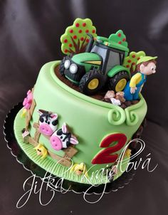 a green cake decorated with farm animals and tractor on it's side, sitting on a black surface