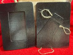 two black frames with twine on them sitting on a red blanket next to a pair of scissors