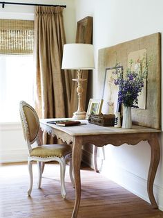 a table with a lamp and pictures on it in front of a window filled with curtains