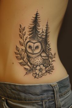 an owl tattoo on the back of a woman's lower body, with trees and flowers around it